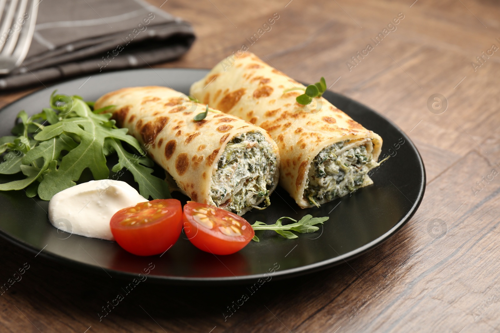 Photo of Tasty rolled crepes with cottage cheese and spinach served on wooden table, closeup