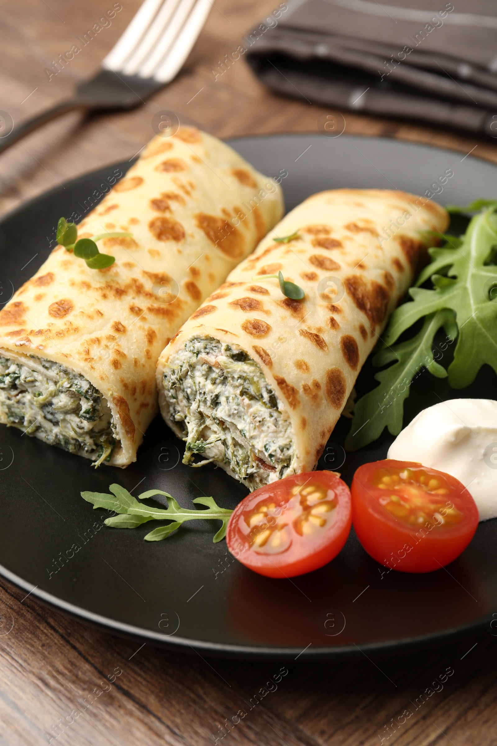 Photo of Tasty rolled crepes with cottage cheese and spinach served on wooden table, closeup