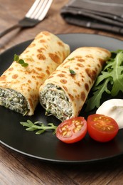 Photo of Tasty rolled crepes with cottage cheese and spinach served on wooden table, closeup