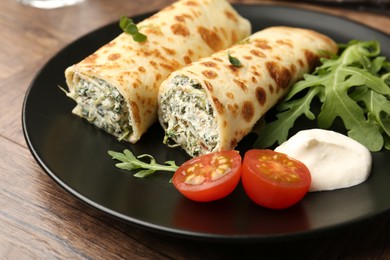 Photo of Tasty rolled crepes with cottage cheese and spinach served on wooden table, closeup