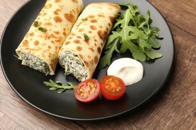 Photo of Tasty rolled crepes with cottage cheese and spinach served on wooden table, closeup