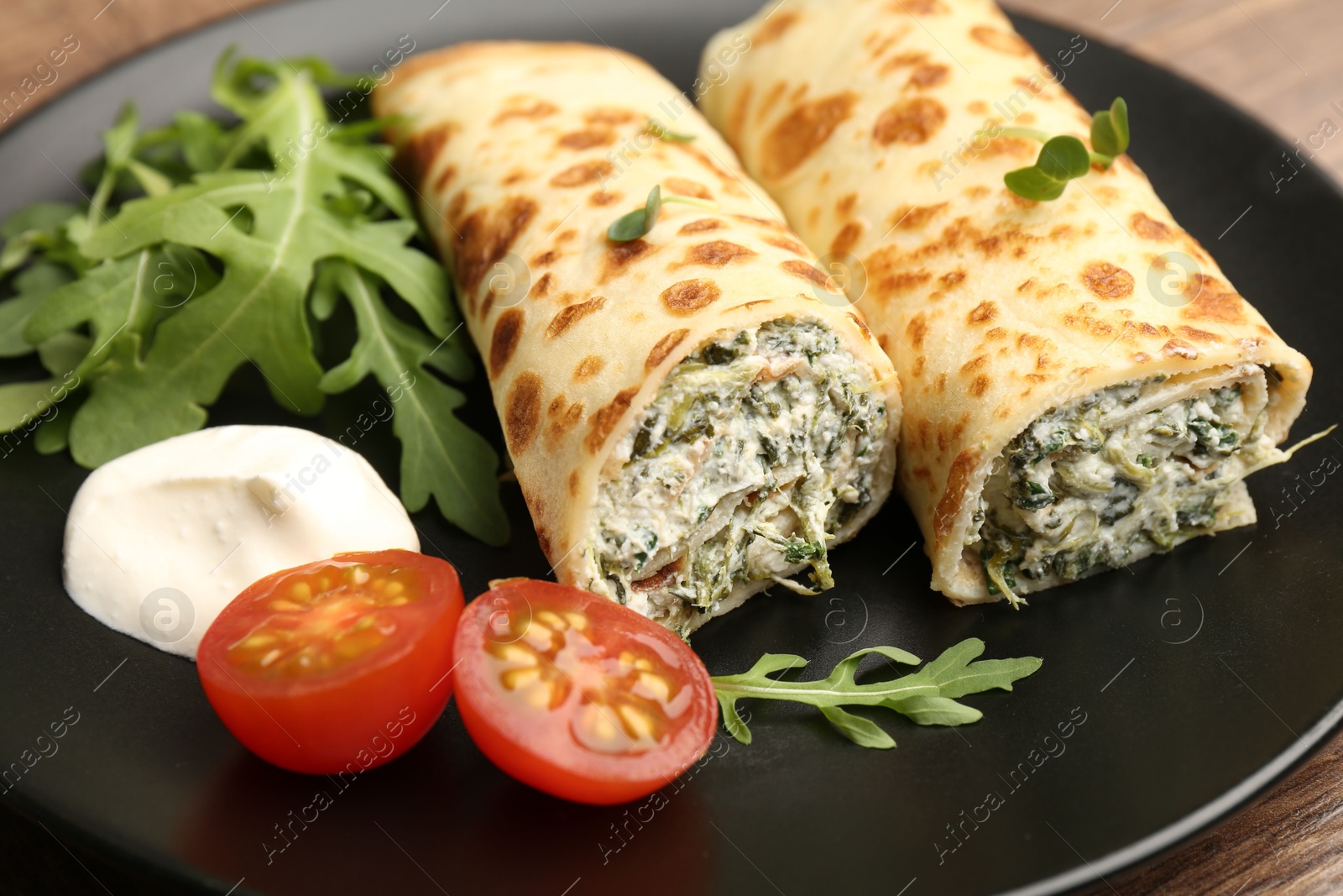 Photo of Tasty rolled crepes with cottage cheese and spinach served on wooden table, closeup