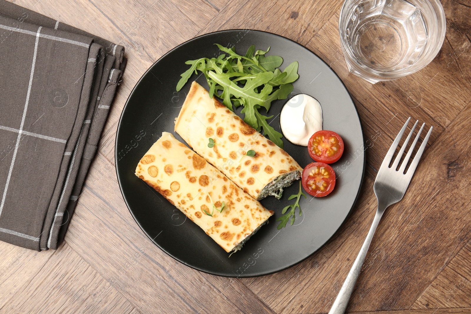 Photo of Tasty rolled crepes with cottage cheese and spinach served on wooden table, flat lay