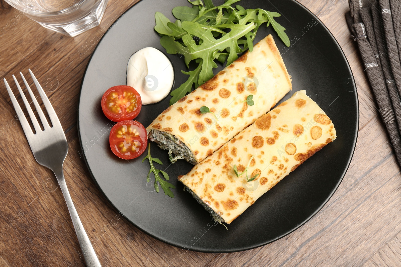 Photo of Tasty rolled crepes with cottage cheese and spinach served on wooden table, flat lay