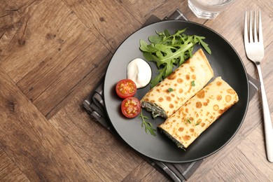 Photo of Tasty rolled crepes with cottage cheese and spinach served on wooden table, flat lay. Space for text