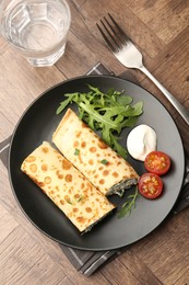 Photo of Tasty rolled crepes with cottage cheese and spinach served on wooden table, flat lay