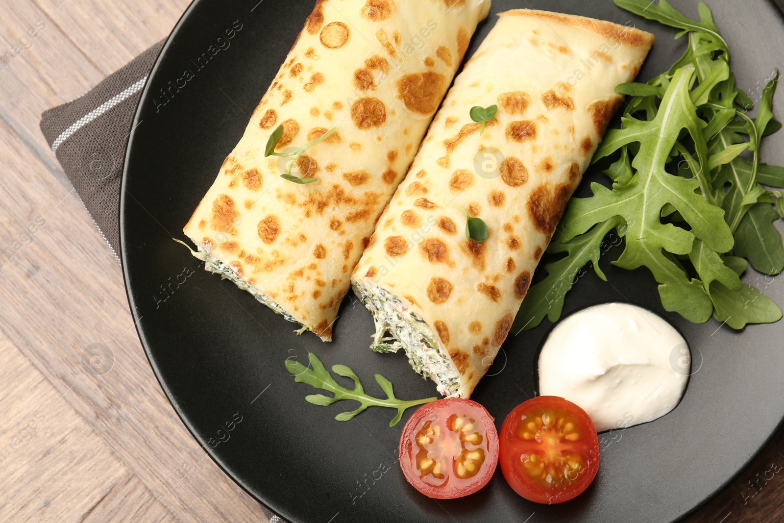 Photo of Tasty rolled crepes with cottage cheese and spinach served on wooden table, top view