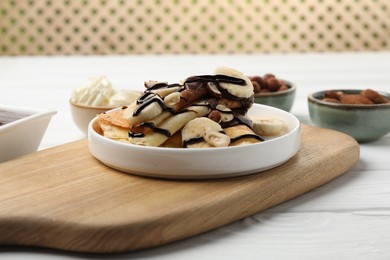 Delicious crepes with banana, nuts, chocolate sauce and whipped cream on white wooden table, closeup