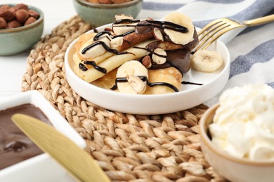 Delicious crepes with banana, chocolate sauce, nuts and whipped cream on table, closeup