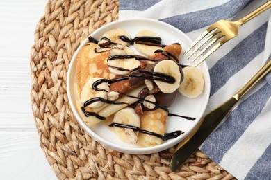 Delicious crepes with banana, chocolate sauce and nuts on white wooden table, top view