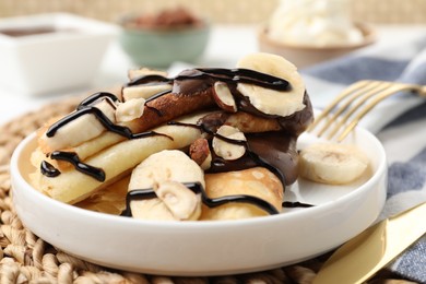 Photo of Delicious crepes with banana, chocolate sauce and nuts on table, closeup