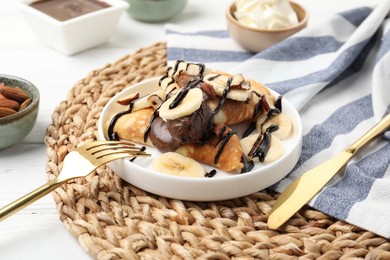 Photo of Delicious crepes with banana, chocolate sauce and nuts on white wooden table, closeup