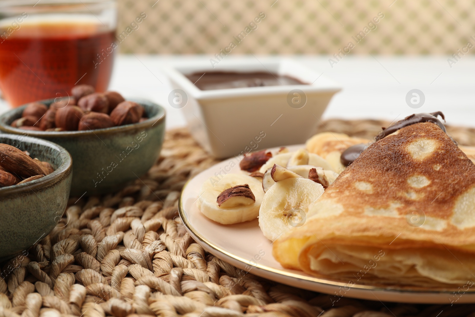 Photo of Delicious crepes with banana, nuts and chocolate paste on table, closeup