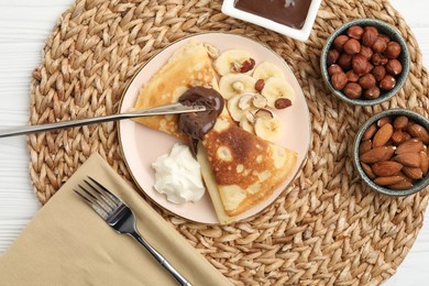 Photo of Delicious crepes with banana, chocolate paste, whipped cream and nuts on white wooden table, flat lay