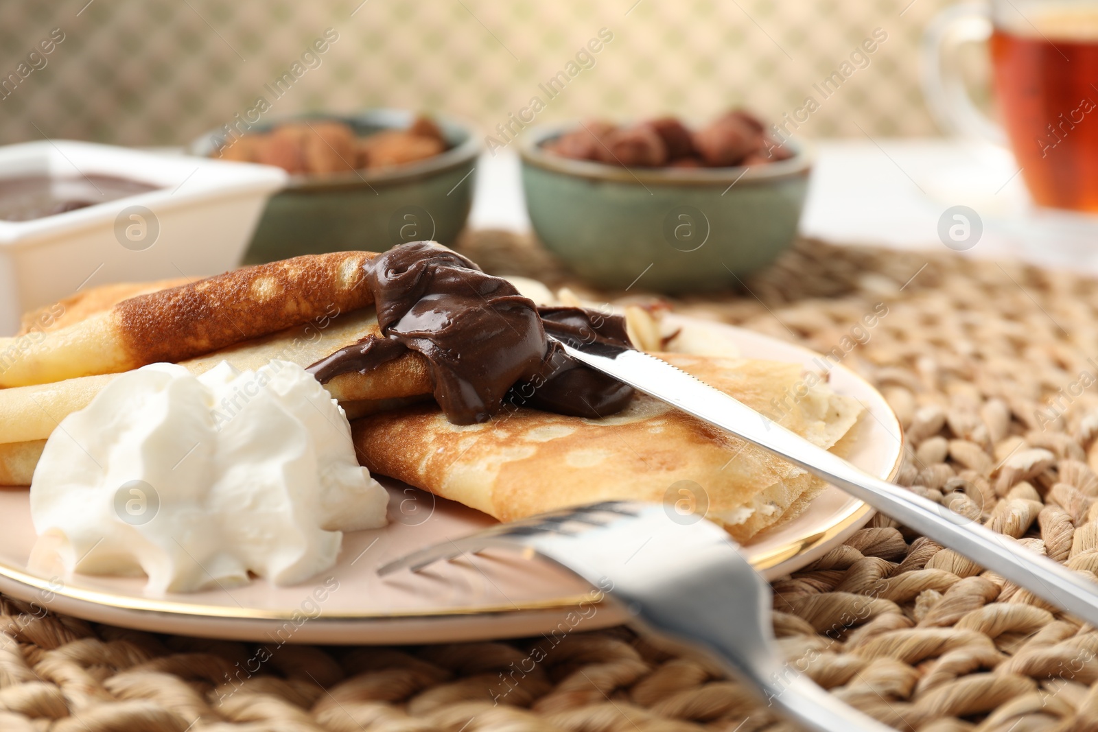 Photo of Delicious crepes with chocolate paste and whipped cream on table, closeup