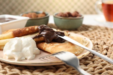 Photo of Delicious crepes with chocolate paste and whipped cream on table, closeup