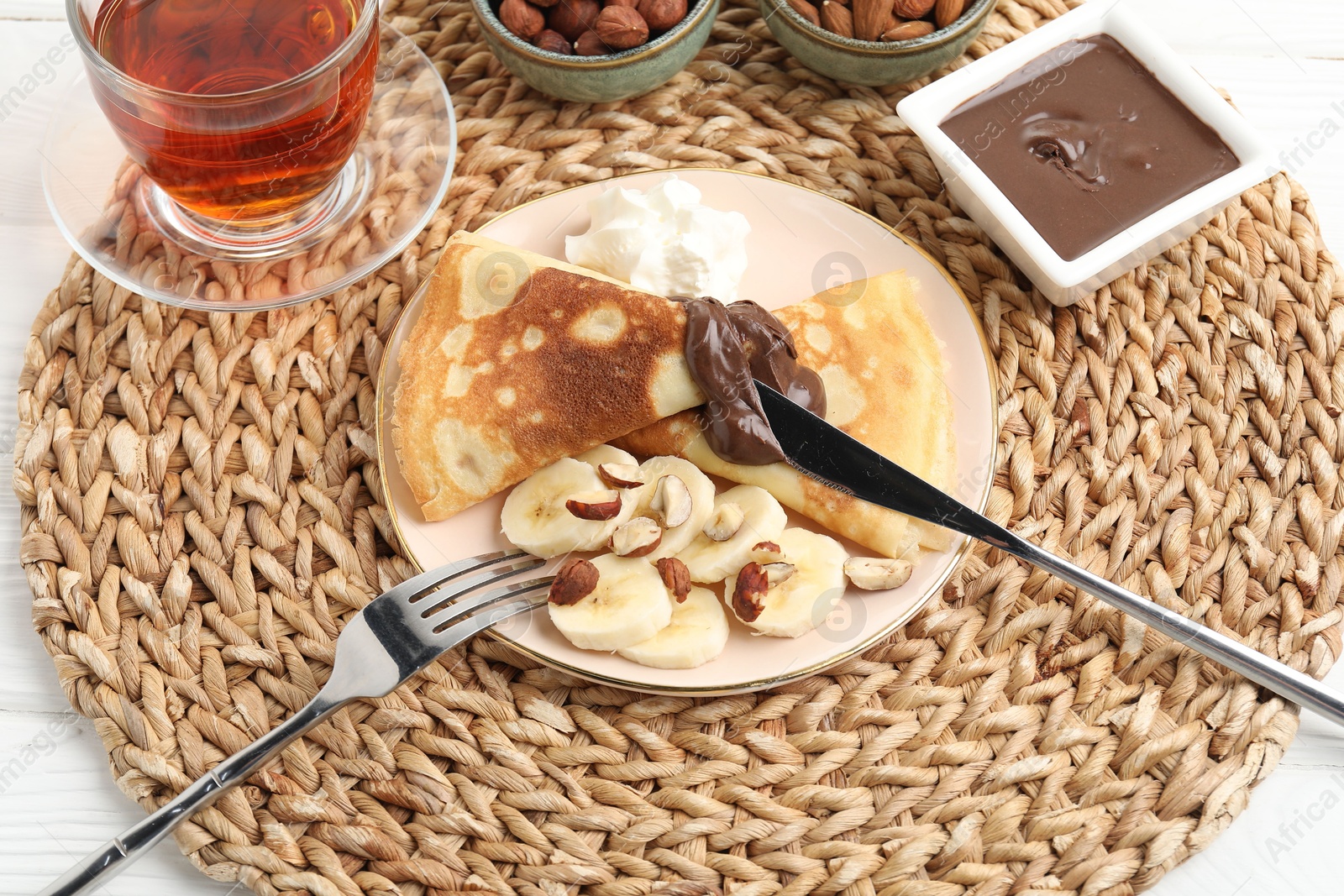 Photo of Delicious crepes with banana, nuts, chocolate paste, whipped cream and tea on table, above view