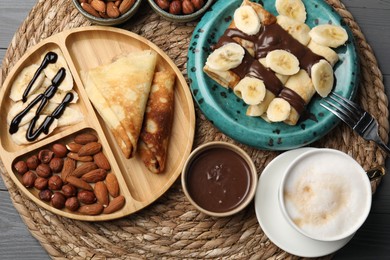 Photo of Delicious crepes served with chocolate paste, nuts and coffee on grey wooden table, flat lay