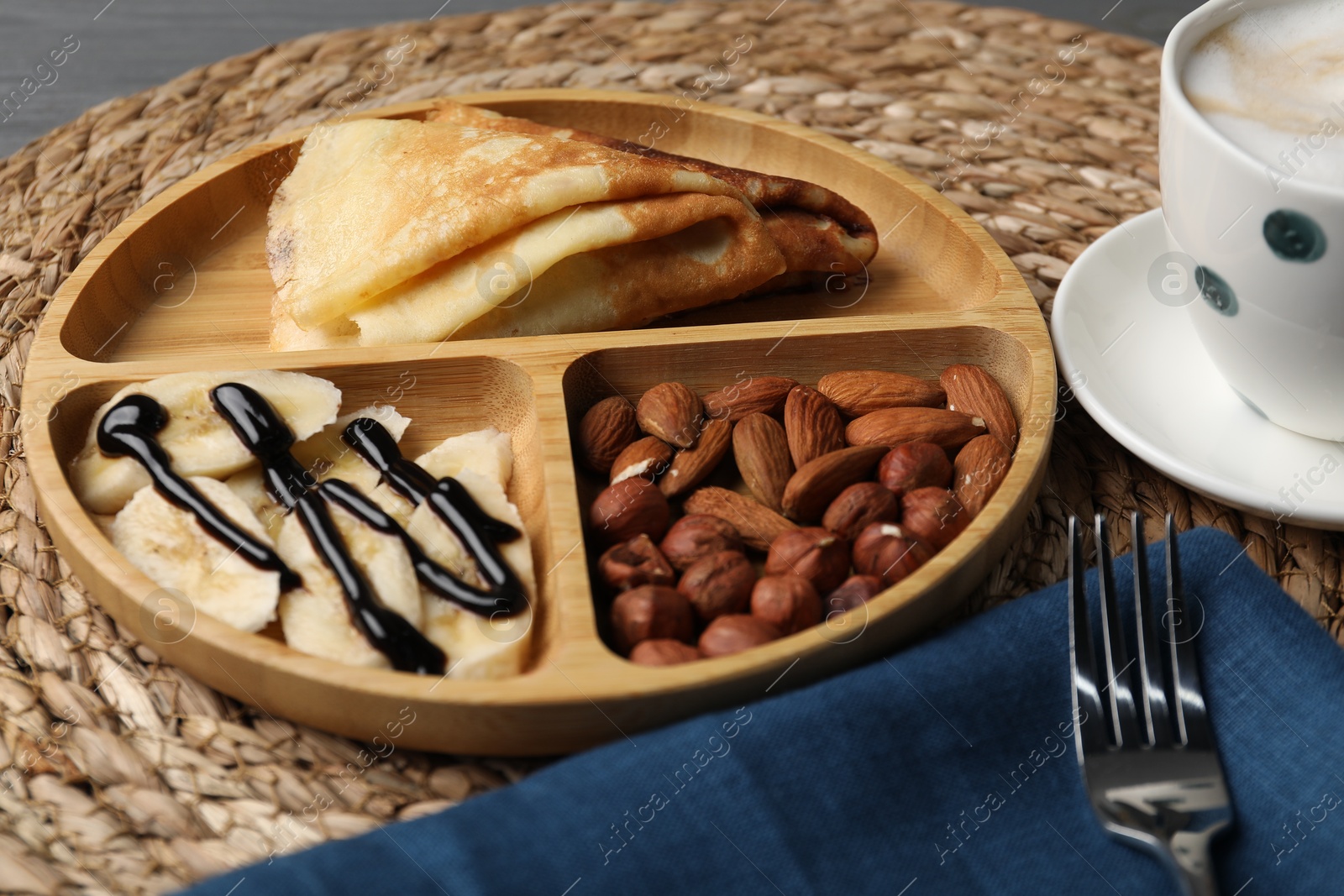 Photo of Delicious crepes with banana, nuts, chocolate sauce and coffee on table, closeup