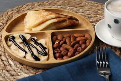 Delicious crepes with banana, nuts, chocolate sauce and coffee on table, closeup