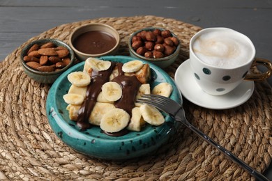 Photo of Delicious crepes with banana, nuts, chocolate paste and coffee on grey wooden table, closeup