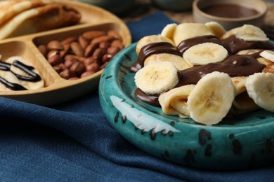 Photo of Delicious crepes with banana, chocolate paste and nuts on table, closeup