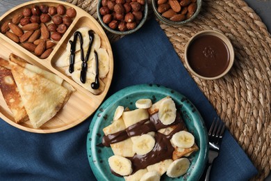 Photo of Delicious crepes served with chocolate paste and nuts on table, flat lay