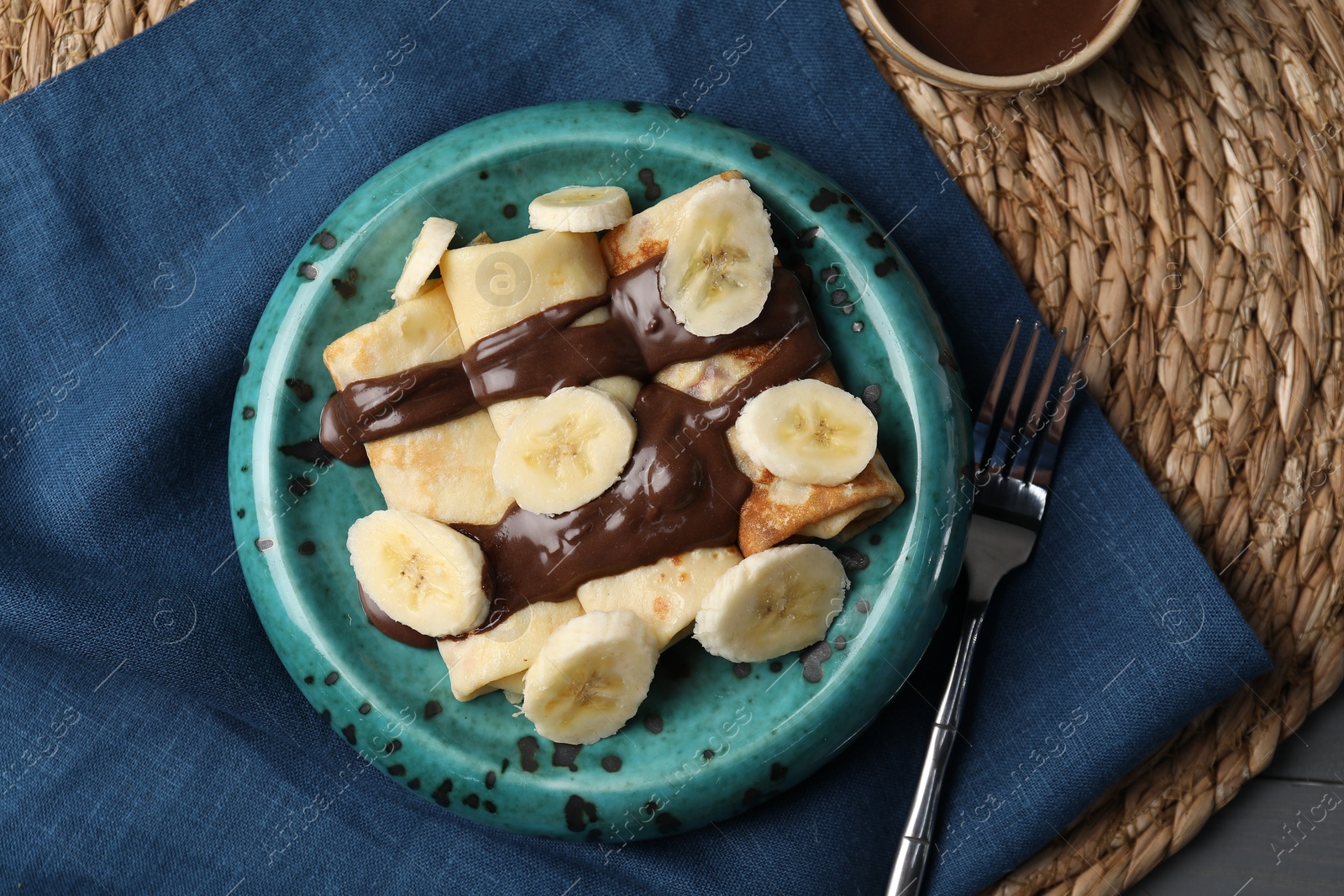 Photo of Delicious crepes with banana and chocolate paste on table, flat lay