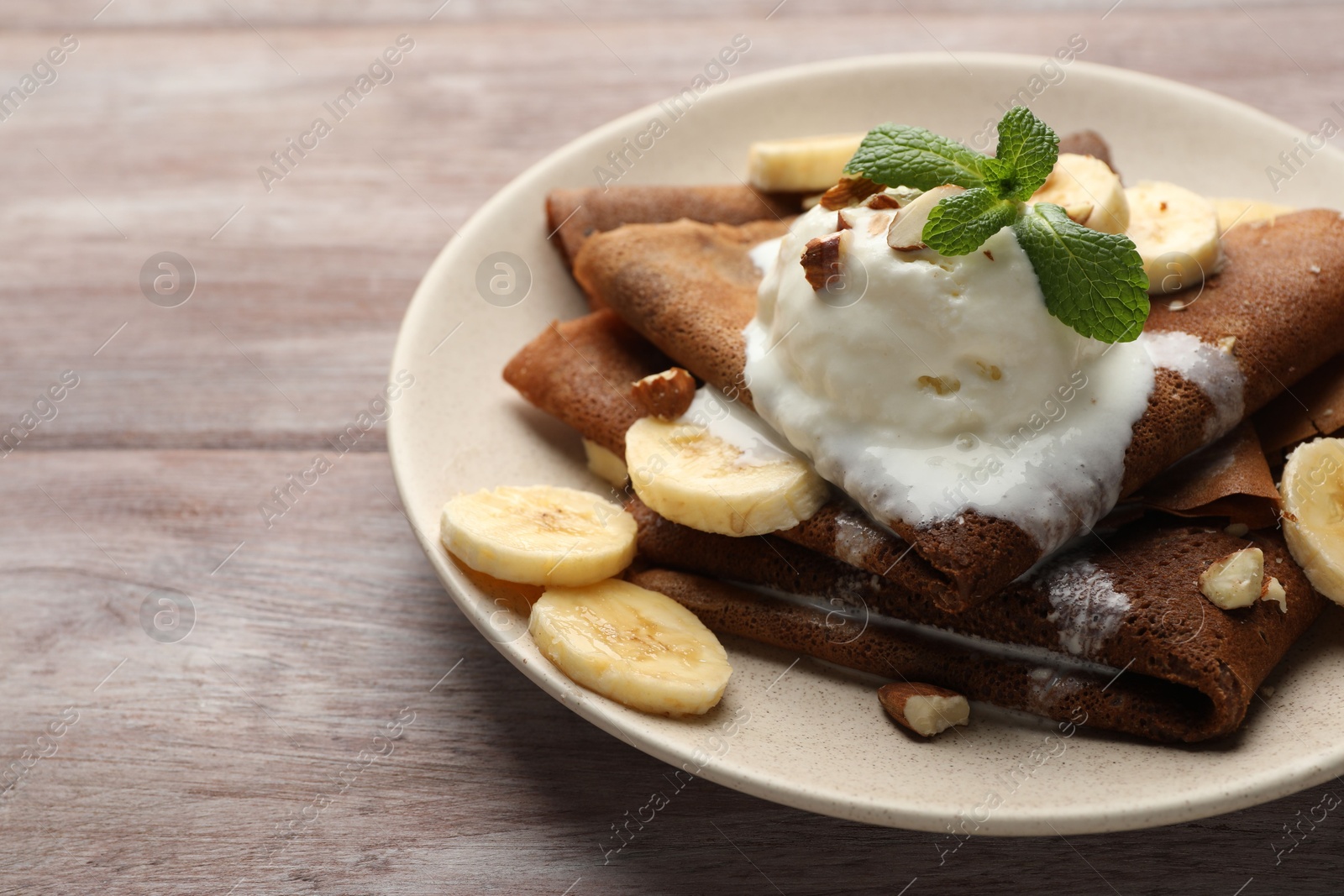 Photo of Delicious chocolate crepes with banana, walnuts, mint and scoop of ice cream on wooden table, closeup. Space for text