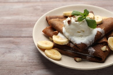 Photo of Delicious chocolate crepes with banana, walnuts, mint and scoop of ice cream on wooden table, closeup. Space for text