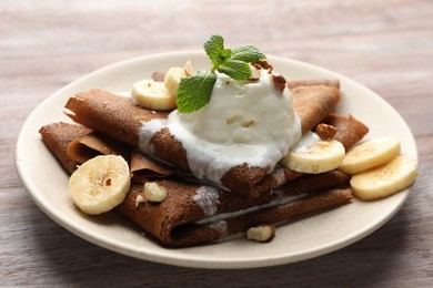 Photo of Delicious chocolate crepes with banana, walnuts, mint and scoop of ice cream on wooden table, closeup