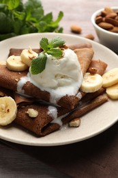 Photo of Delicious chocolate crepes with banana, nuts, mint and scoop of ice cream on wooden table, closeup