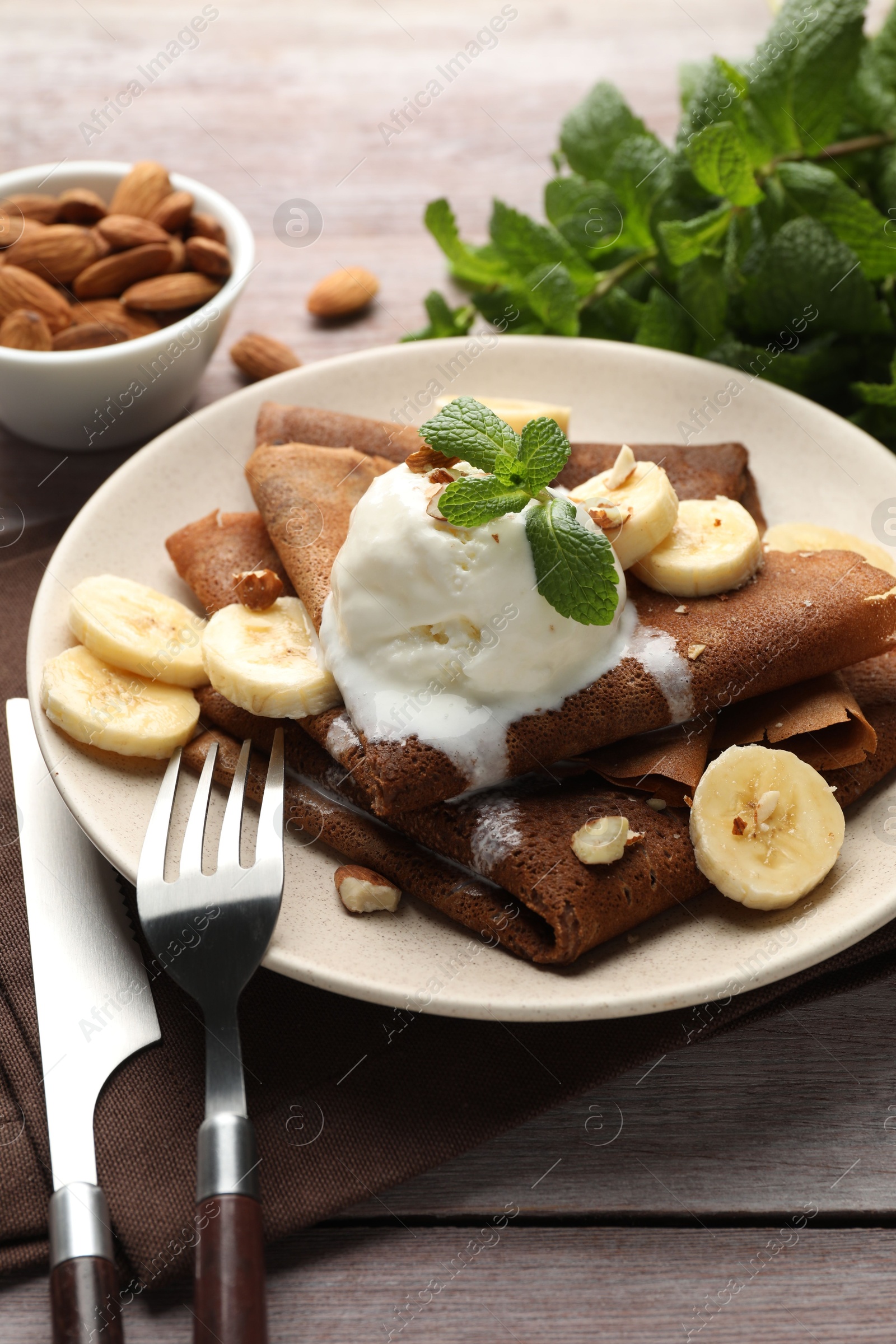 Photo of Delicious chocolate crepes with banana, nuts, mint and scoop of ice cream on wooden table, closeup