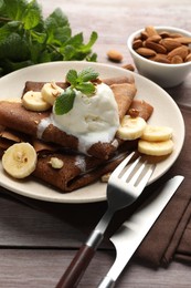 Photo of Delicious chocolate crepes with banana, nuts, mint and scoop of ice cream on wooden table, closeup