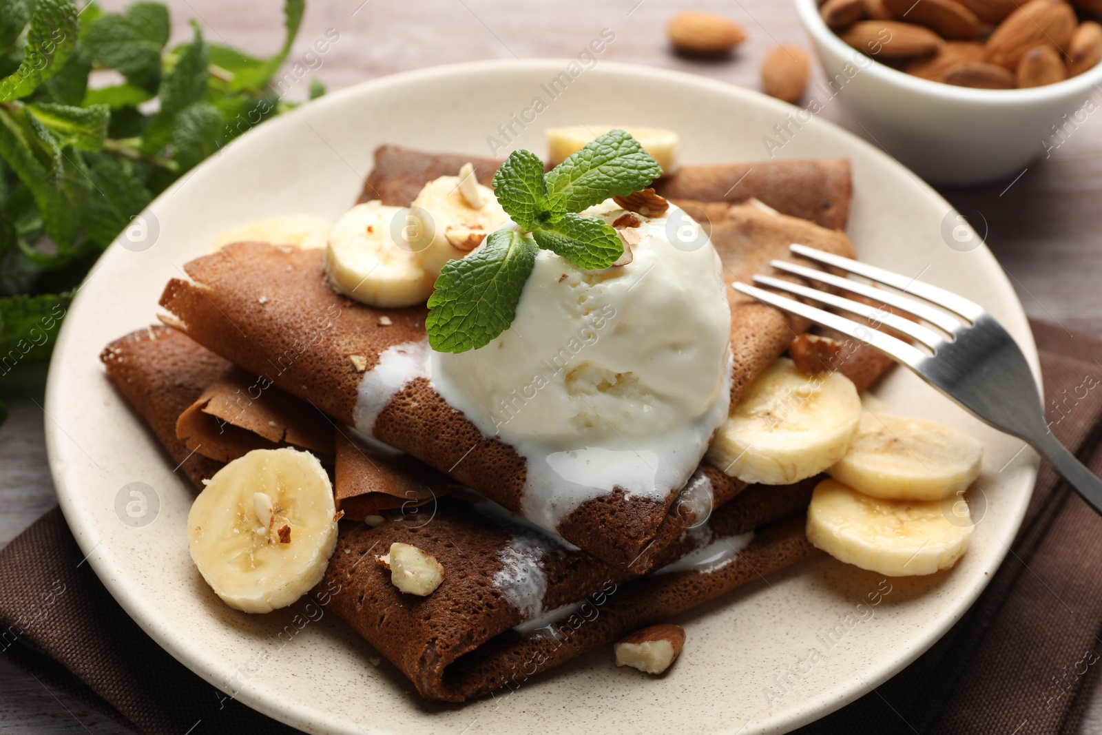 Photo of Delicious chocolate crepes with banana, nuts, mint and scoop of ice cream on table, closeup