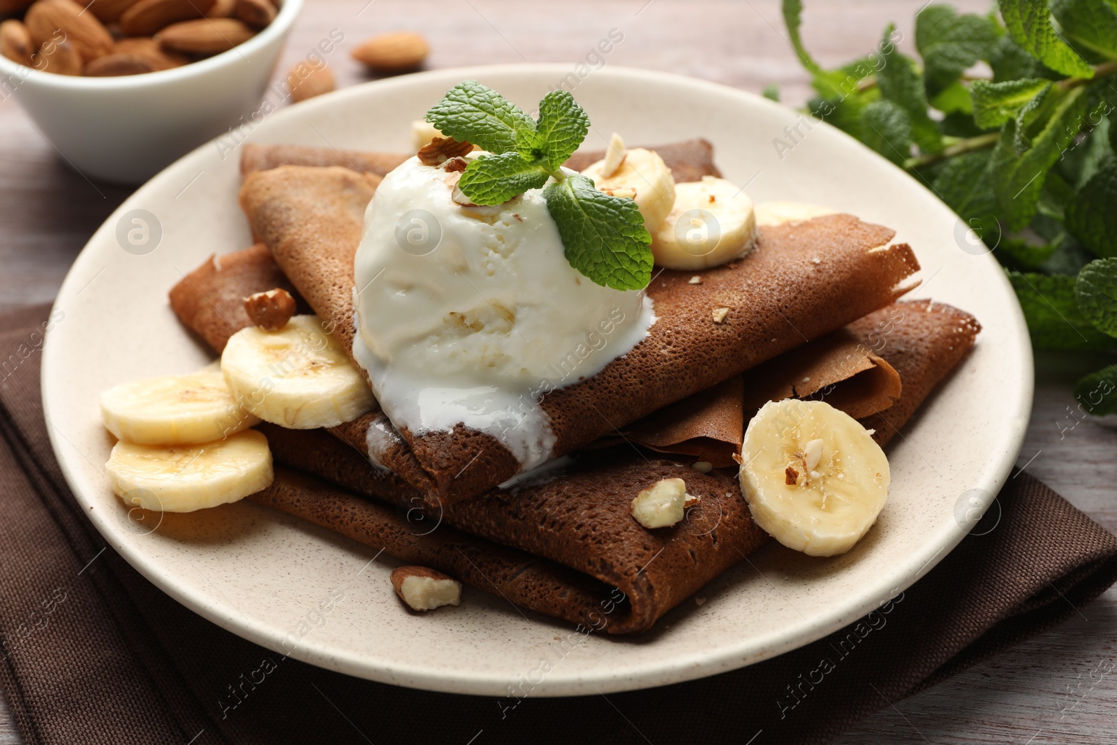 Photo of Delicious chocolate crepes with banana, nuts, mint and scoop of ice cream on wooden table, closeup