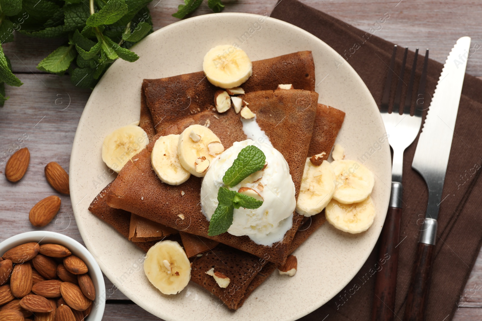 Photo of Delicious chocolate crepes with banana, nuts, mint and scoop of ice cream on wooden table, flat lay