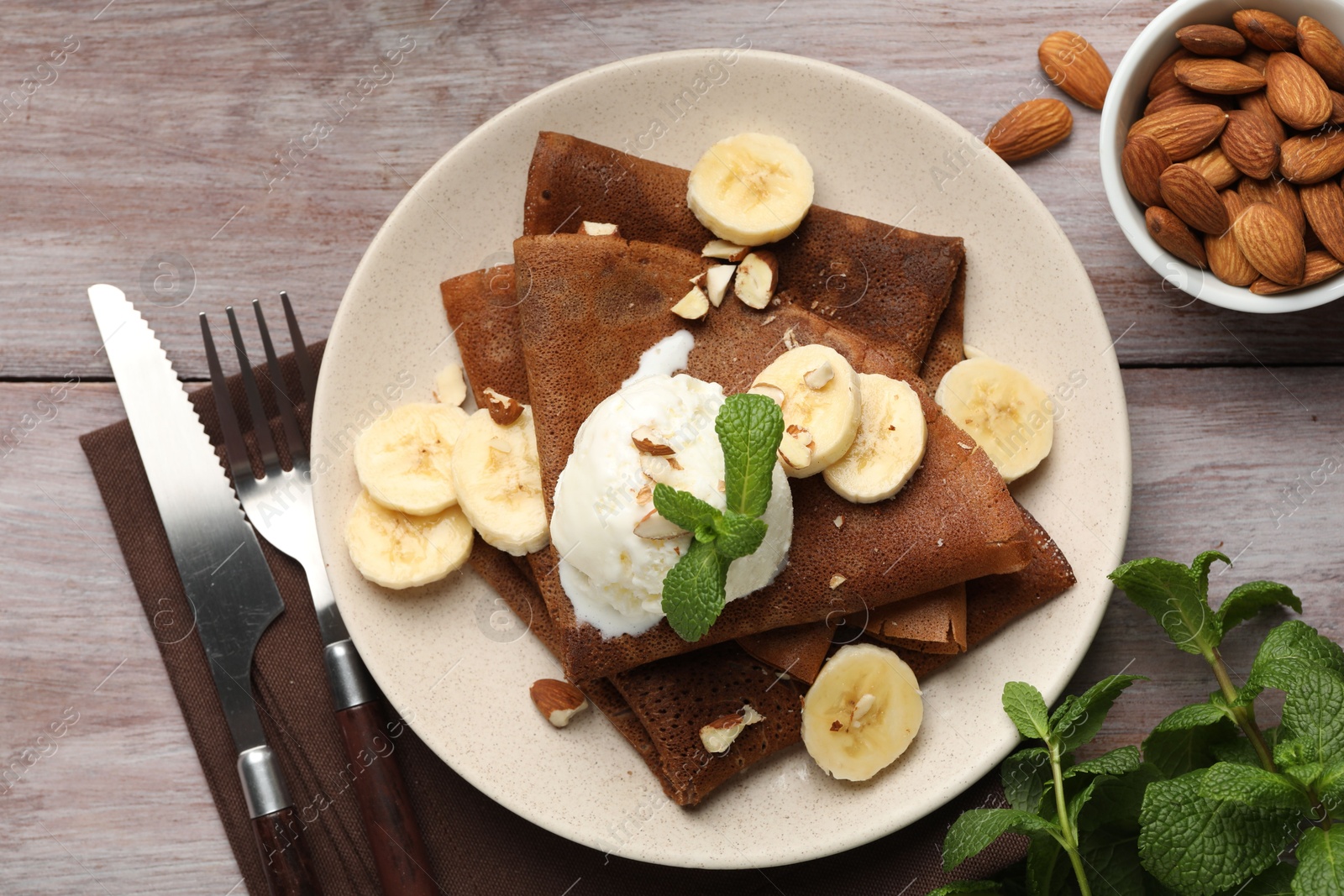 Photo of Delicious chocolate crepes with banana, nuts, mint and scoop of ice cream on wooden table, flat lay