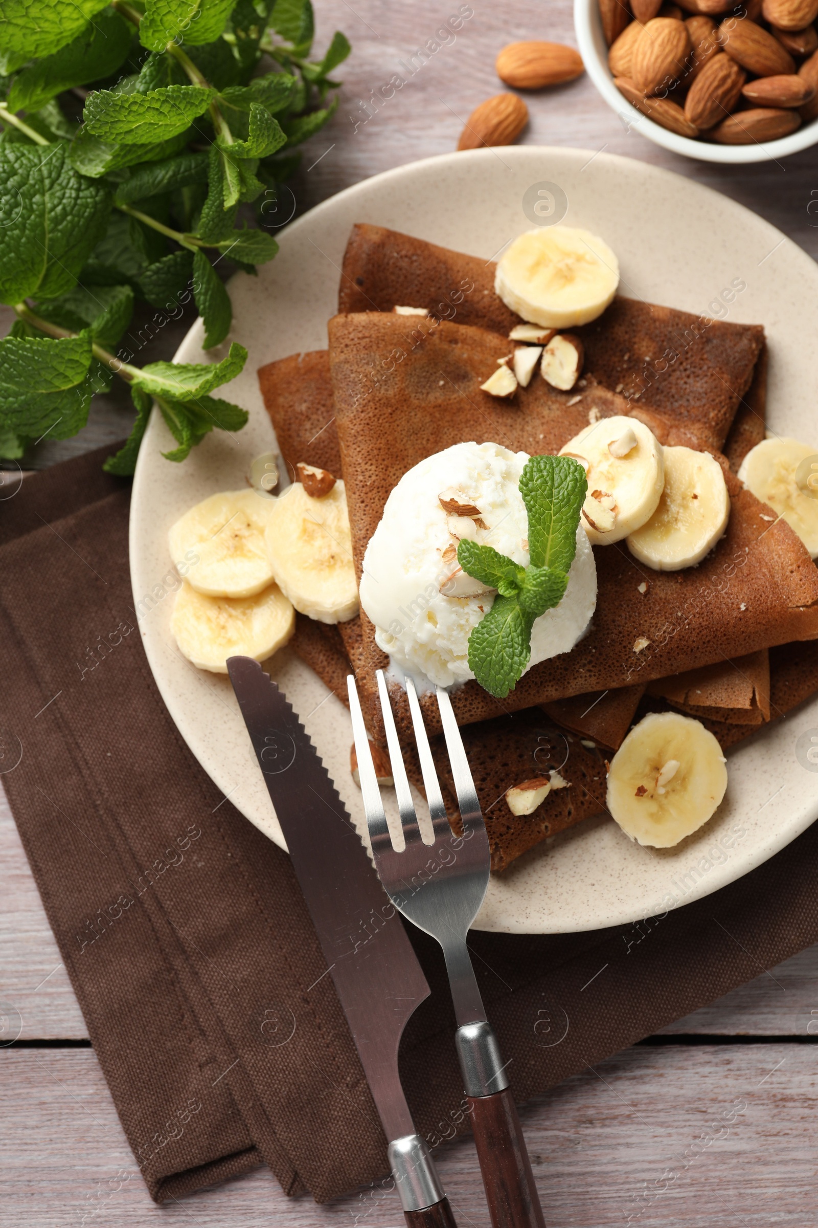 Photo of Delicious chocolate crepes with banana, nuts, mint and scoop of ice cream on wooden table, flat lay