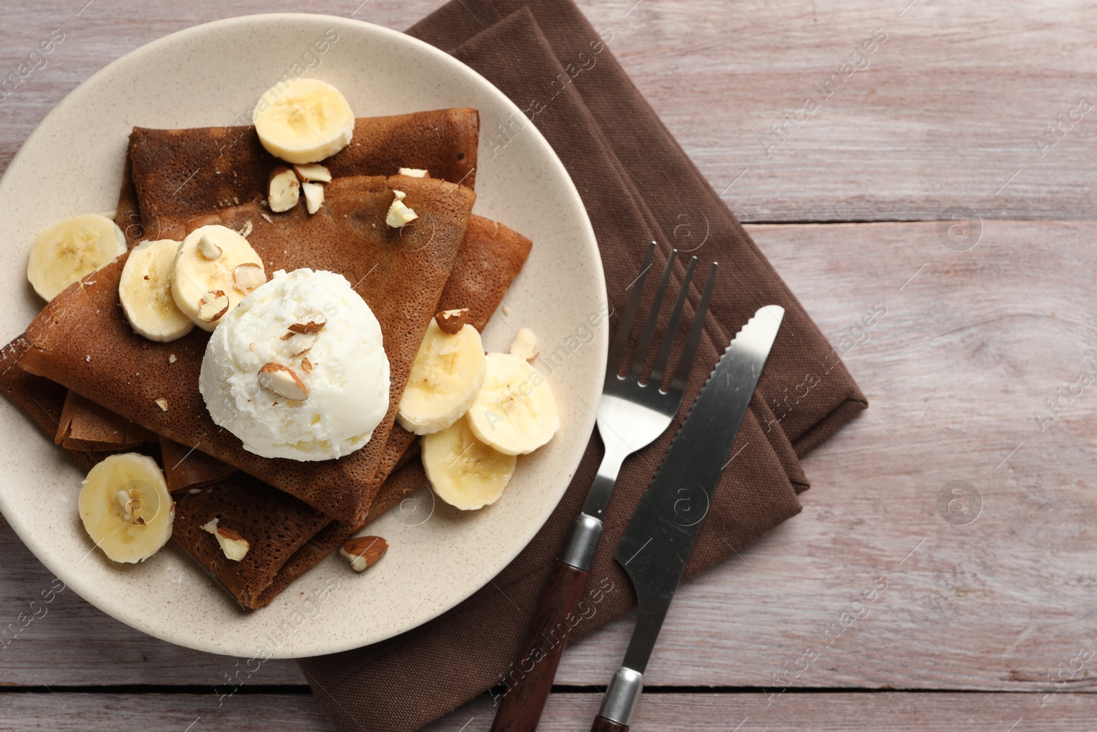 Photo of Delicious chocolate crepes with banana, nuts and scoop of ice cream on wooden table, flat lay. Space for text