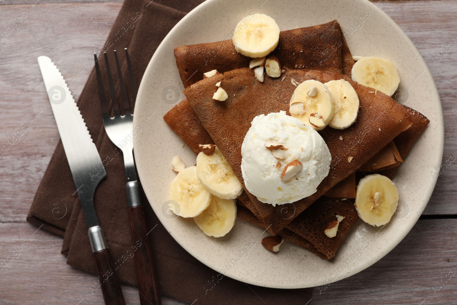 Photo of Delicious chocolate crepes with banana, nuts and scoop of ice cream on wooden table, flat lay