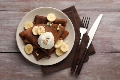 Photo of Delicious chocolate crepes with banana, nuts and scoop of ice cream on wooden table, flat lay