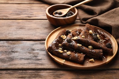 Photo of Delicious chocolate crepes with pine cone jam and nuts on wooden table, closeup. Space for text