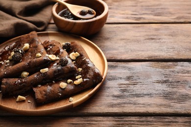 Photo of Delicious chocolate crepes with pine cone jam and nuts on wooden table, closeup. Space for text