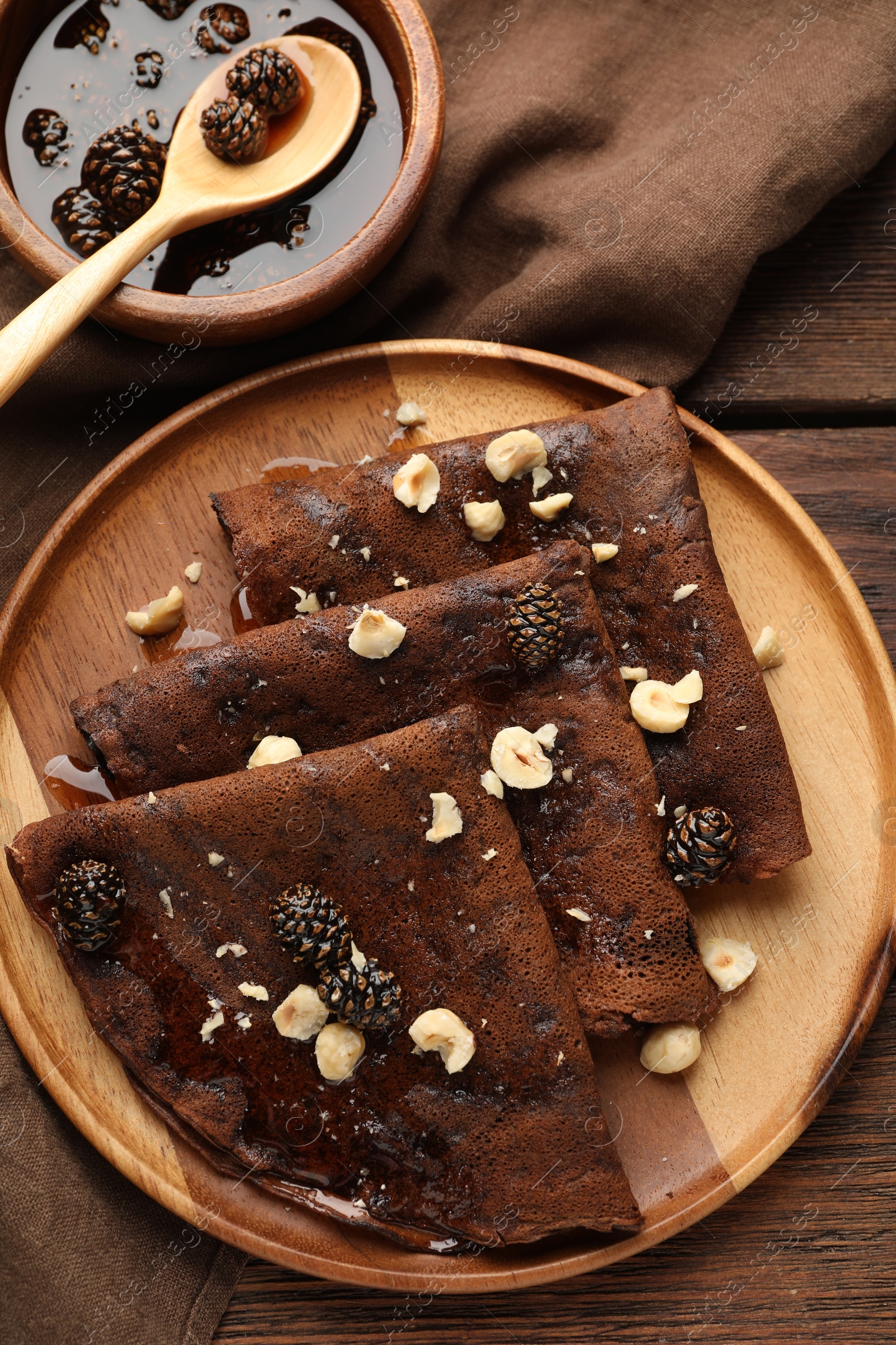 Photo of Delicious chocolate crepes with pine cone jam and nuts on wooden table, flat lay