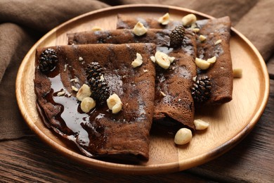 Photo of Delicious chocolate crepes with pine cone jam and nuts on wooden table, closeup