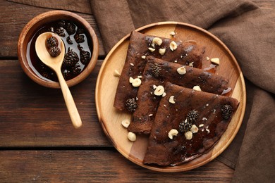 Photo of Delicious chocolate crepes with pine cone jam and nuts on wooden table, flat lay