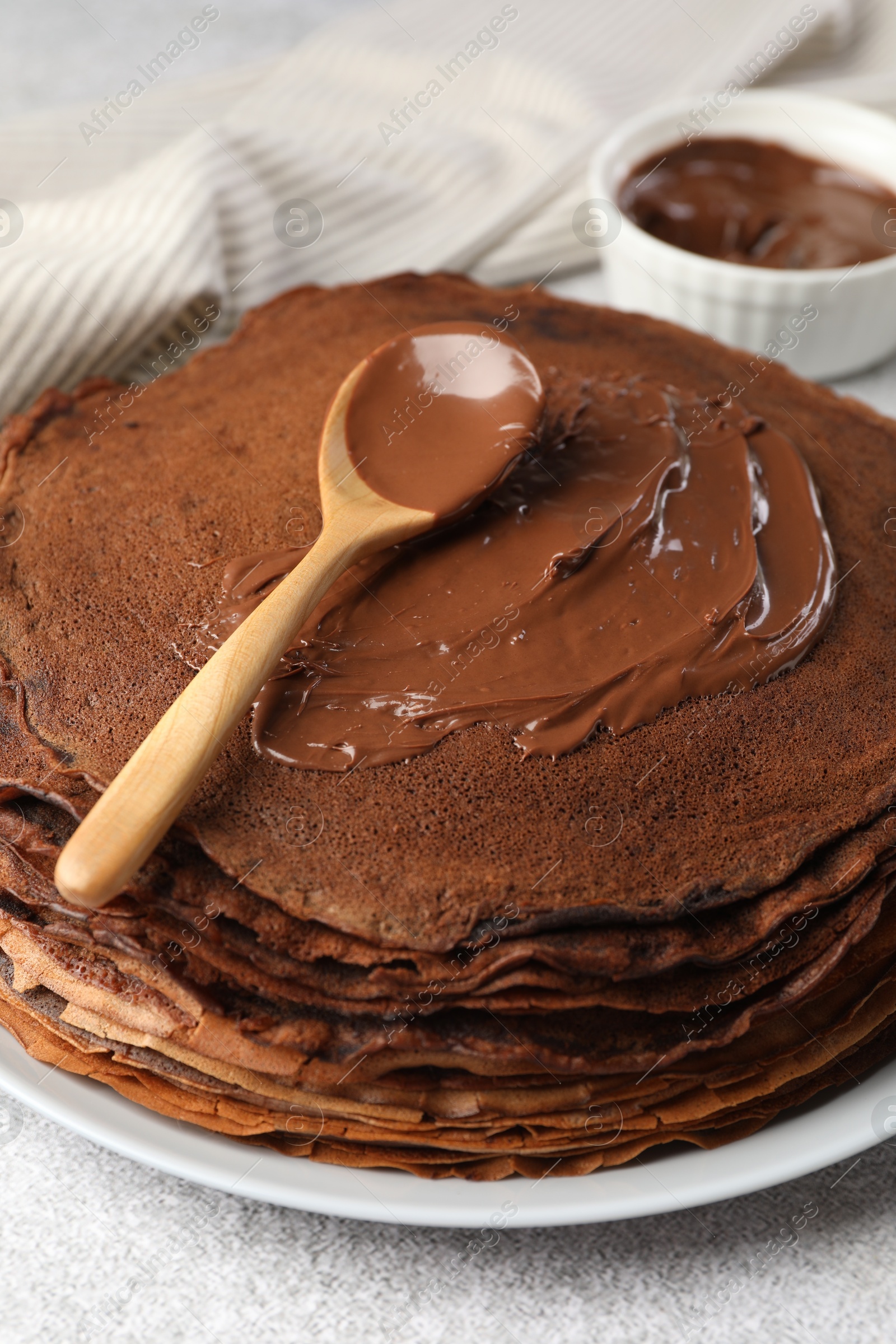 Photo of Delicious chocolate crepes with sweet paste on light grey table, closeup