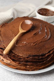 Photo of Delicious chocolate crepes with sweet paste on light grey table, closeup