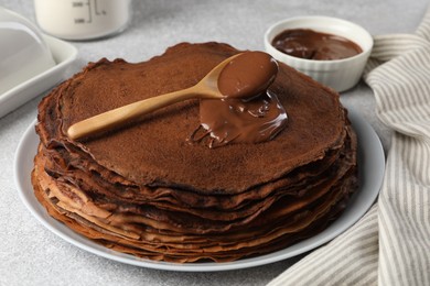 Photo of Delicious chocolate crepes with sweet paste on light grey table, closeup